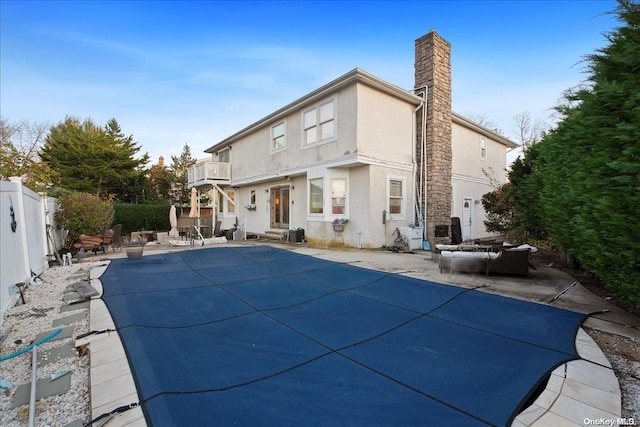 rear view of property with a balcony, a covered pool, and a patio area