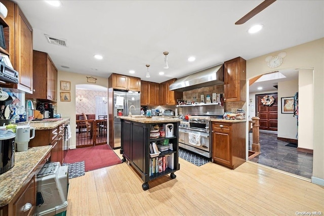 kitchen with light hardwood / wood-style flooring, a kitchen island, wall chimney range hood, and appliances with stainless steel finishes