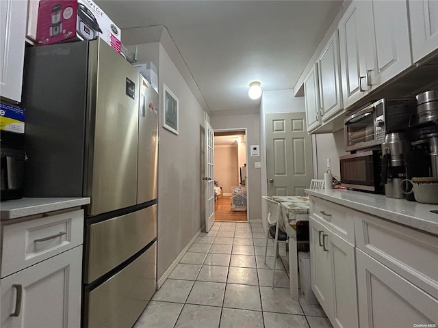 kitchen with light tile patterned flooring, light stone counters, stainless steel appliances, and white cabinetry