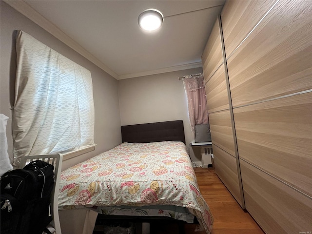 bedroom with radiator heating unit, light hardwood / wood-style flooring, and ornamental molding