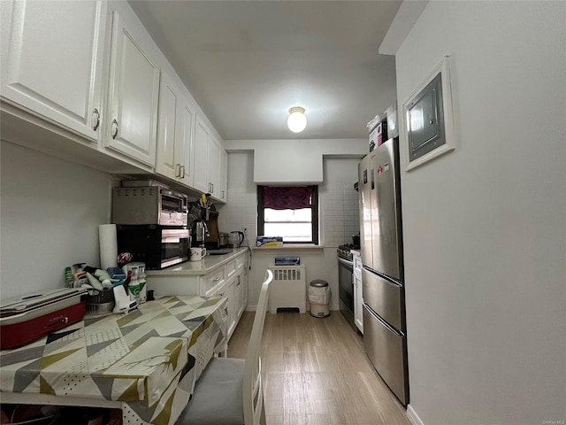 kitchen with stainless steel appliances, radiator, light countertops, light wood-style floors, and white cabinets