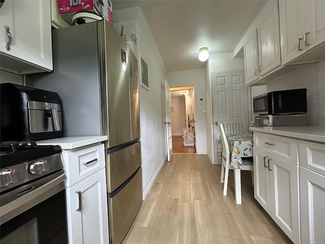 13 W Mill Dr Unit 3A, Great Neck, NY 11021 - kitchen with stainless steel range with gas stovetop, light countertops, white cabinets, black microwave, and light wood-style floors