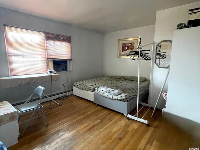 bedroom featuring cooling unit, wood-type flooring, and a baseboard heating unit