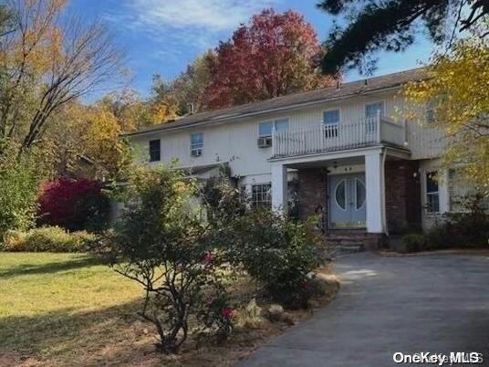 view of front of house featuring a front yard, a balcony, and a wall mounted AC