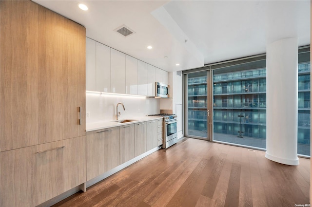 kitchen with appliances with stainless steel finishes, light brown cabinetry, sink, hardwood / wood-style flooring, and a wall of windows