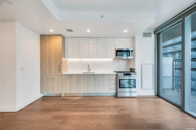 kitchen with appliances with stainless steel finishes, light hardwood / wood-style floors, white cabinetry, and sink