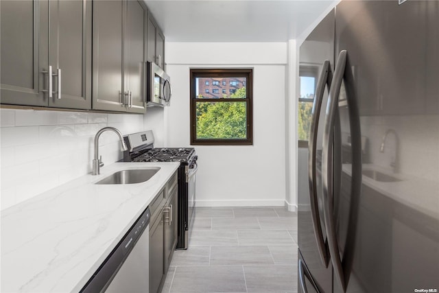 kitchen featuring gray cabinetry, sink, decorative backsplash, light stone countertops, and stainless steel appliances