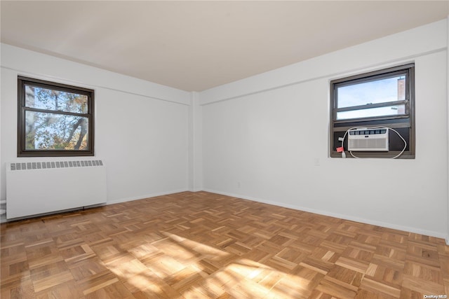 empty room featuring a wealth of natural light, cooling unit, radiator, and light parquet floors