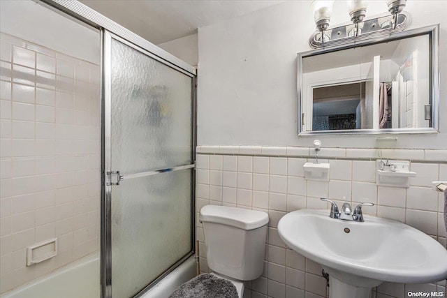 full bathroom featuring toilet, bath / shower combo with glass door, sink, and tile walls