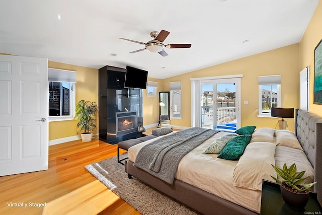 bedroom featuring vaulted ceiling, access to outside, ceiling fan, a fireplace, and hardwood / wood-style floors