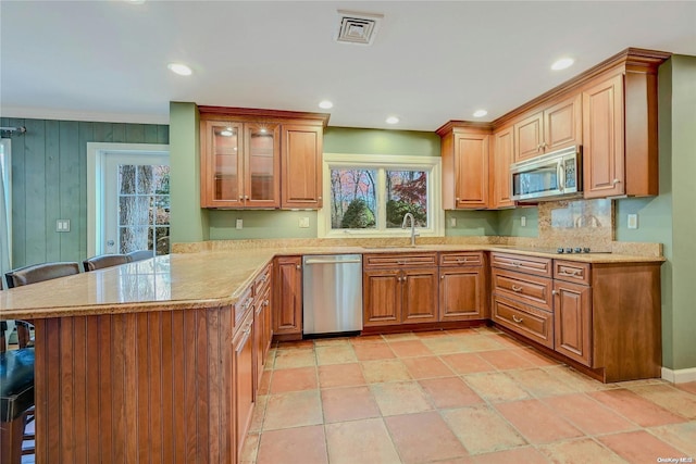 kitchen with sink, stainless steel appliances, kitchen peninsula, wood walls, and a kitchen bar