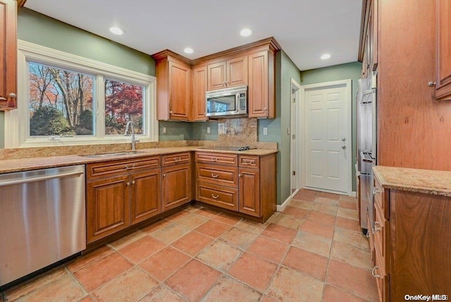 kitchen with decorative backsplash, sink, light stone countertops, and appliances with stainless steel finishes