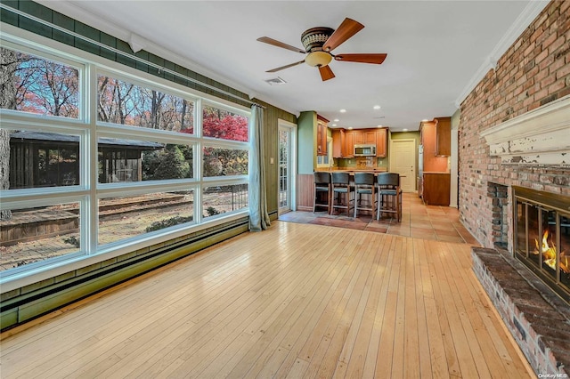 unfurnished living room featuring light hardwood / wood-style floors, a brick fireplace, ceiling fan, and crown molding