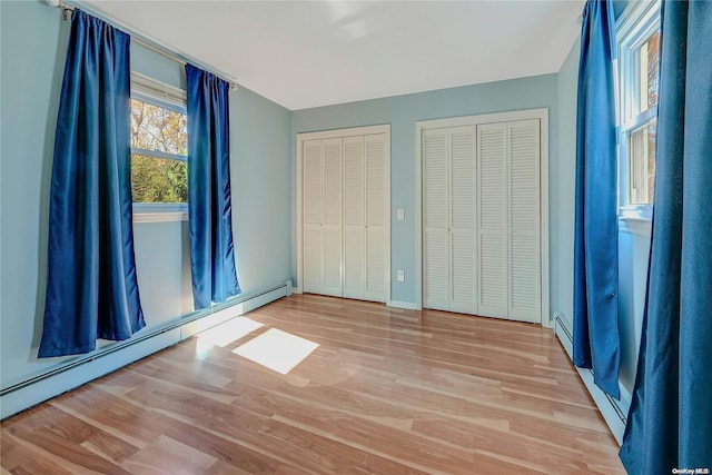 unfurnished bedroom featuring light wood-type flooring, two closets, and a baseboard heating unit