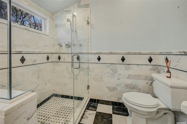 bathroom featuring lofted ceiling, toilet, a shower with door, and tile walls