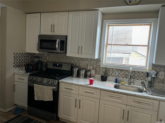 kitchen with appliances with stainless steel finishes, backsplash, white cabinetry, and sink