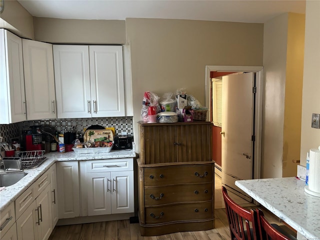 kitchen with light stone counters, white cabinetry, backsplash, and light hardwood / wood-style flooring