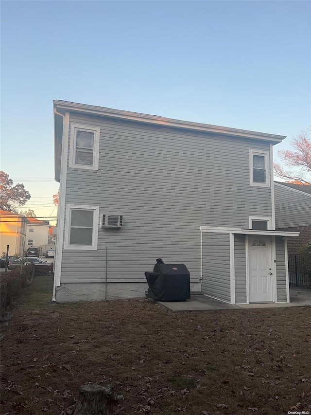 back house at dusk with a wall mounted air conditioner