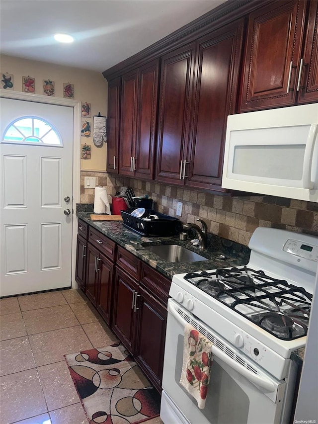 kitchen with sink, tasteful backsplash, dark stone countertops, white appliances, and light tile patterned flooring