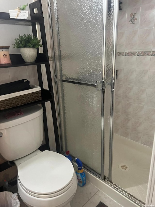 bathroom with tile patterned flooring, a shower with shower door, and toilet