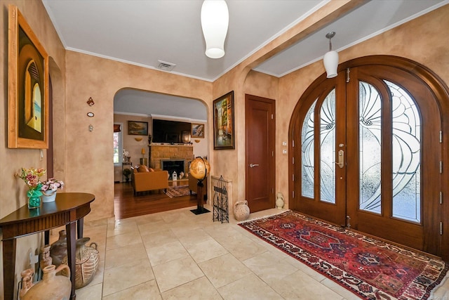 entryway with arched walkways, a fireplace, visible vents, french doors, and ornamental molding