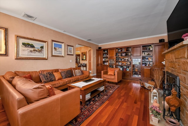 living room with arched walkways, a stone fireplace, visible vents, ornamental molding, and dark wood finished floors