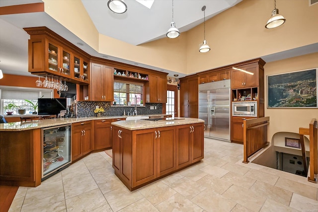 kitchen featuring wine cooler, a center island, backsplash, light stone countertops, and built in appliances