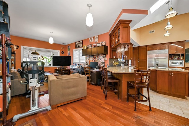 kitchen with light wood finished floors, visible vents, brown cabinetry, built in appliances, and a sink