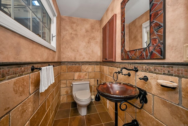 half bathroom featuring wainscoting, toilet, a sink, tile patterned flooring, and tile walls