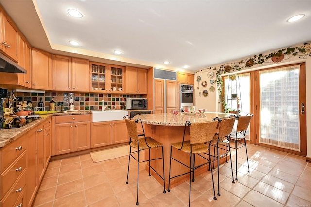 kitchen with black electric stovetop, wall oven, a breakfast bar, a sink, and glass insert cabinets