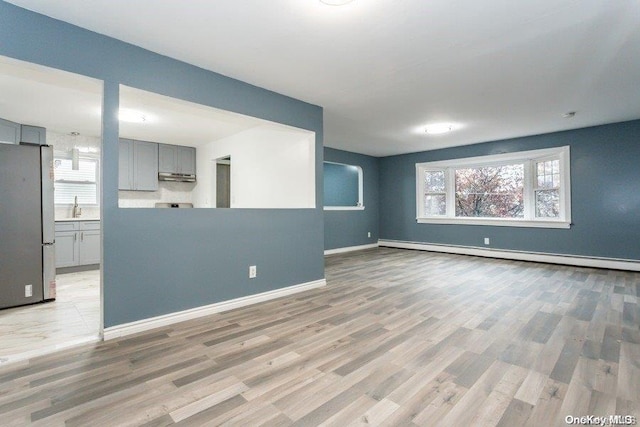 unfurnished living room with baseboard heating, light hardwood / wood-style flooring, and sink