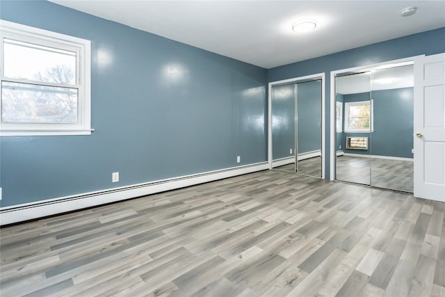 unfurnished bedroom featuring two closets, light hardwood / wood-style floors, and multiple windows