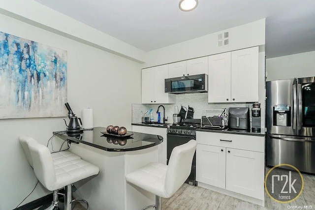 kitchen with black appliances, white cabinets, decorative backsplash, light hardwood / wood-style floors, and a kitchen bar