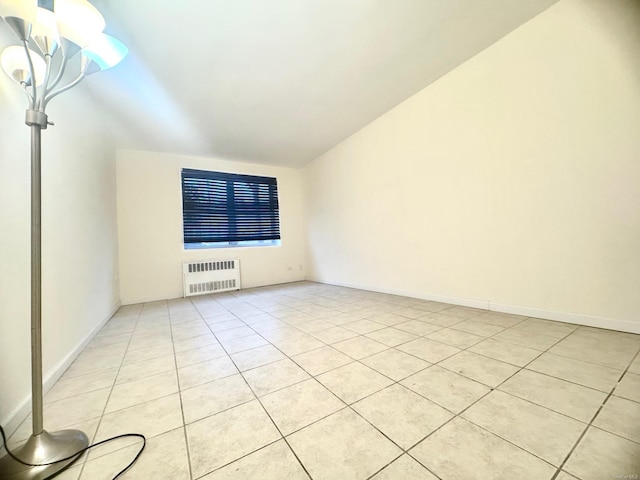 tiled empty room featuring radiator and vaulted ceiling