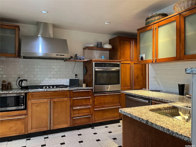 kitchen featuring backsplash, light stone countertops, wall chimney exhaust hood, and stainless steel appliances