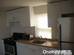 kitchen with stainless steel refrigerator, white cabinetry, sink, range with electric stovetop, and exhaust hood