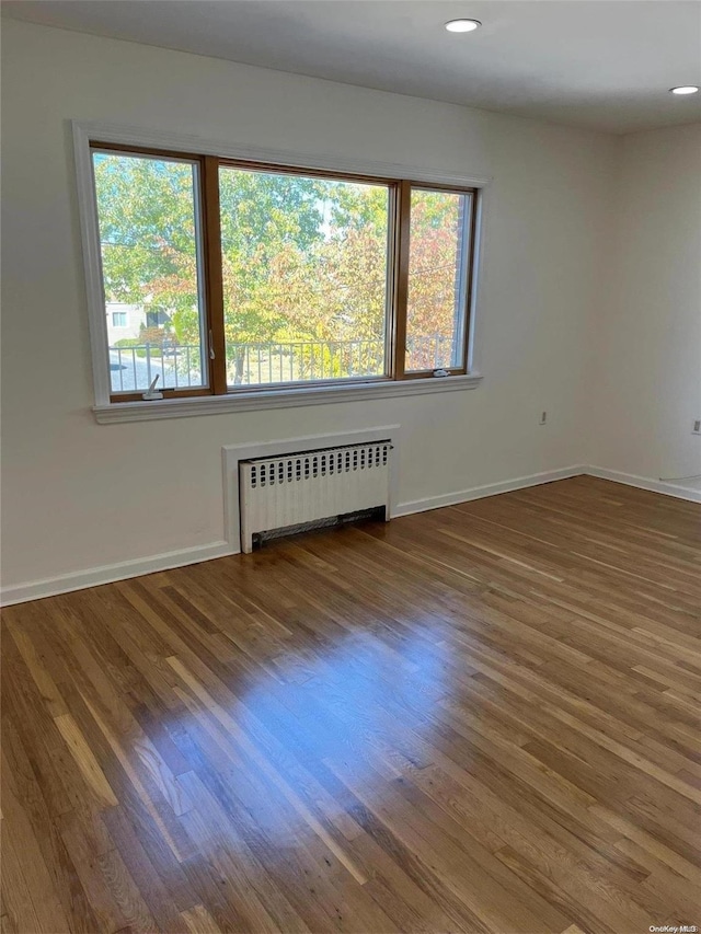 empty room with hardwood / wood-style floors, radiator heating unit, and a wealth of natural light