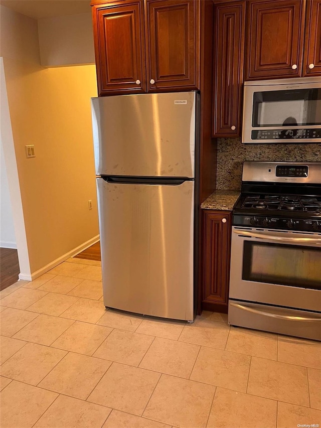 kitchen with decorative backsplash, light tile patterned floors, stainless steel appliances, and dark stone counters