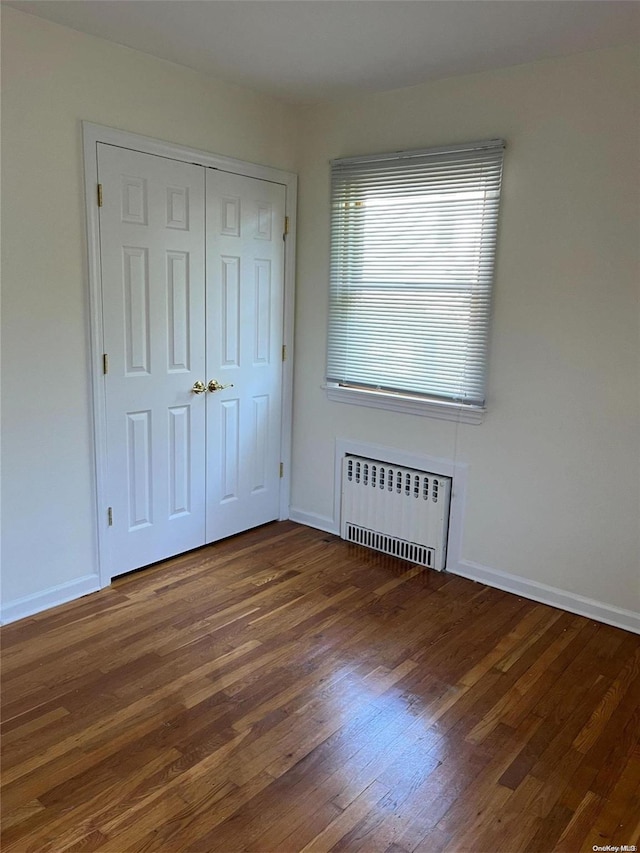 unfurnished bedroom featuring dark hardwood / wood-style flooring, radiator heating unit, and a closet