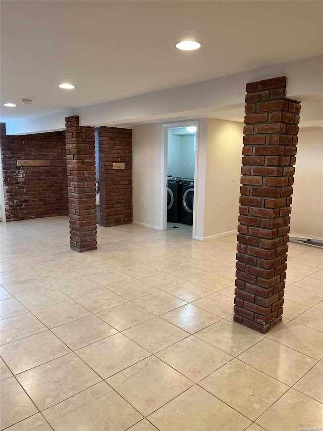 basement featuring light tile patterned floors, washing machine and dryer, and brick wall