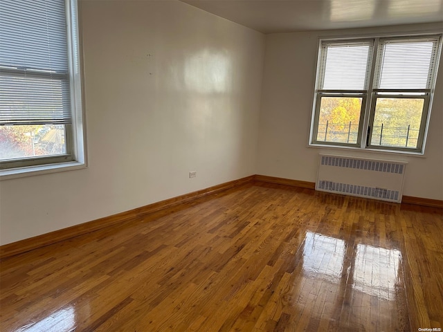 unfurnished room with wood-type flooring, radiator heating unit, and a healthy amount of sunlight