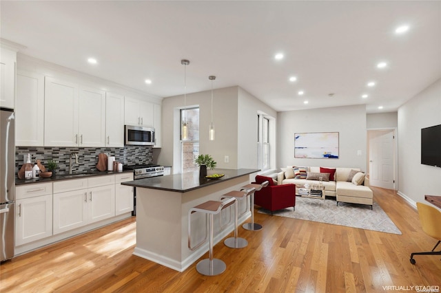 kitchen featuring white cabinetry, hanging light fixtures, appliances with stainless steel finishes, and light hardwood / wood-style flooring