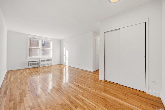 interior space with wood-type flooring, radiator heating unit, a wall mounted AC, and a closet