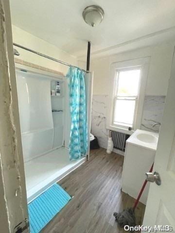 bathroom featuring hardwood / wood-style floors, vanity, walk in shower, and radiator