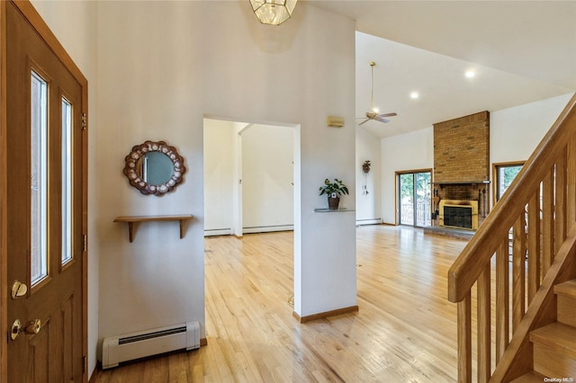 entryway featuring ceiling fan with notable chandelier, light hardwood / wood-style flooring, a towering ceiling, a fireplace, and baseboard heating