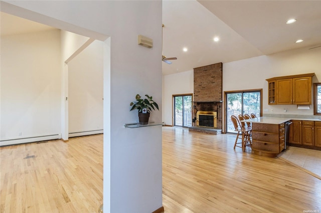 kitchen with ceiling fan, light wood-type flooring, high vaulted ceiling, and a brick fireplace