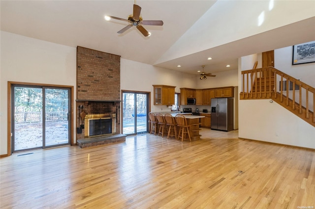 living room featuring a wealth of natural light, light hardwood / wood-style flooring, high vaulted ceiling, and a brick fireplace