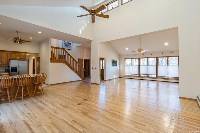 living room featuring ceiling fan, light wood-type flooring, high vaulted ceiling, and a baseboard heating unit