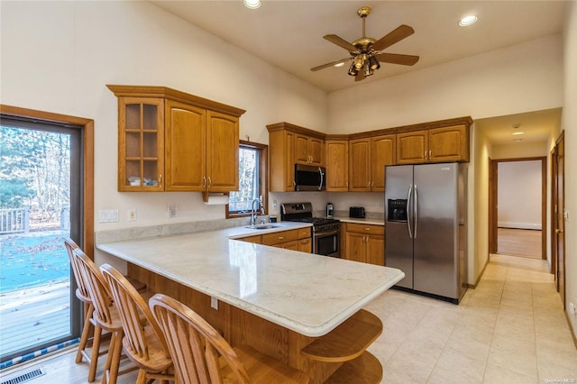 kitchen with kitchen peninsula, appliances with stainless steel finishes, a breakfast bar, ceiling fan, and sink