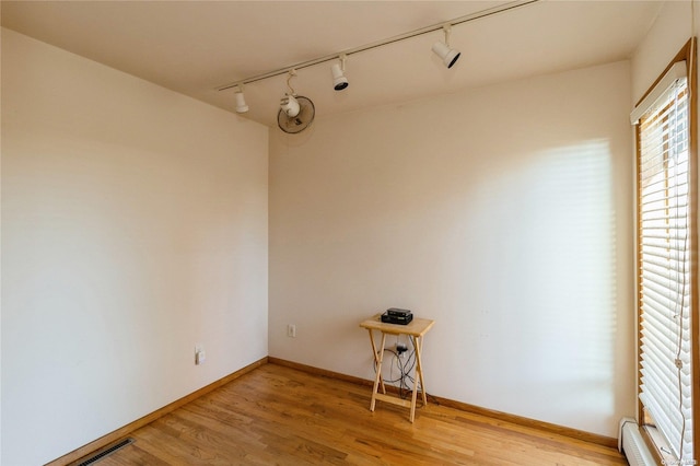 unfurnished room featuring hardwood / wood-style floors, baseboard heating, and rail lighting